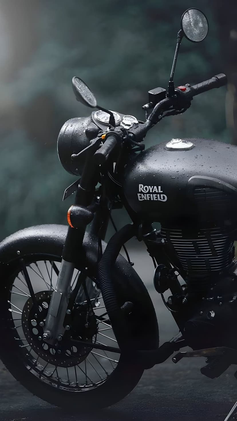 Royal Enfield motorcycle fuel tank features glistening water droplets on matte black paint in the rain.