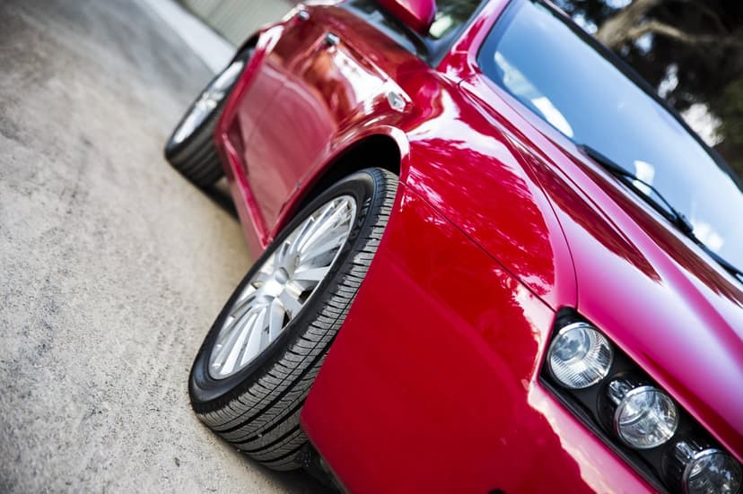 Red sports car wheel featuring a multi-spoke alloy rim, tire tread, and glossy fender with light reflections.