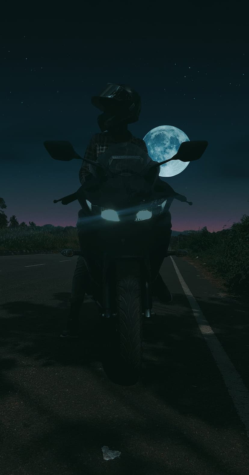 Motorcyclist in silhouette travels along a dark road toward a massive, bright full moon in a starry night sky.