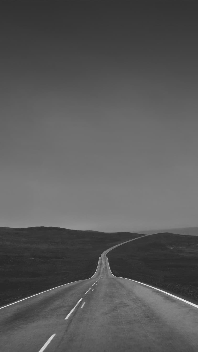 Straight paved road stretching toward a flat horizon between rolling hills in a stark black and white landscape.