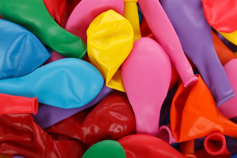 Uninflated party balloons in various bright colors including green and red bunched together in a textured pile.