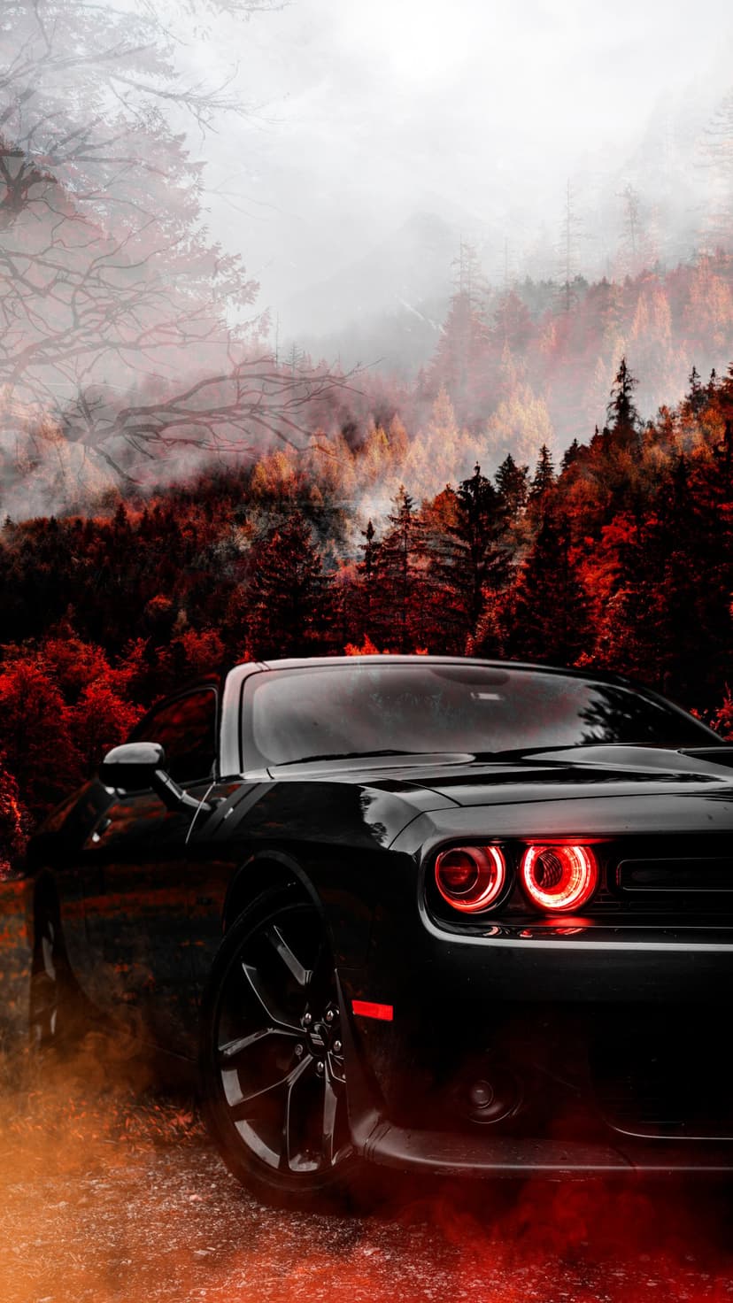 Black Dodge Challenger with glowing red headlights on a foggy gravel road lined with vibrant autumn foliage.