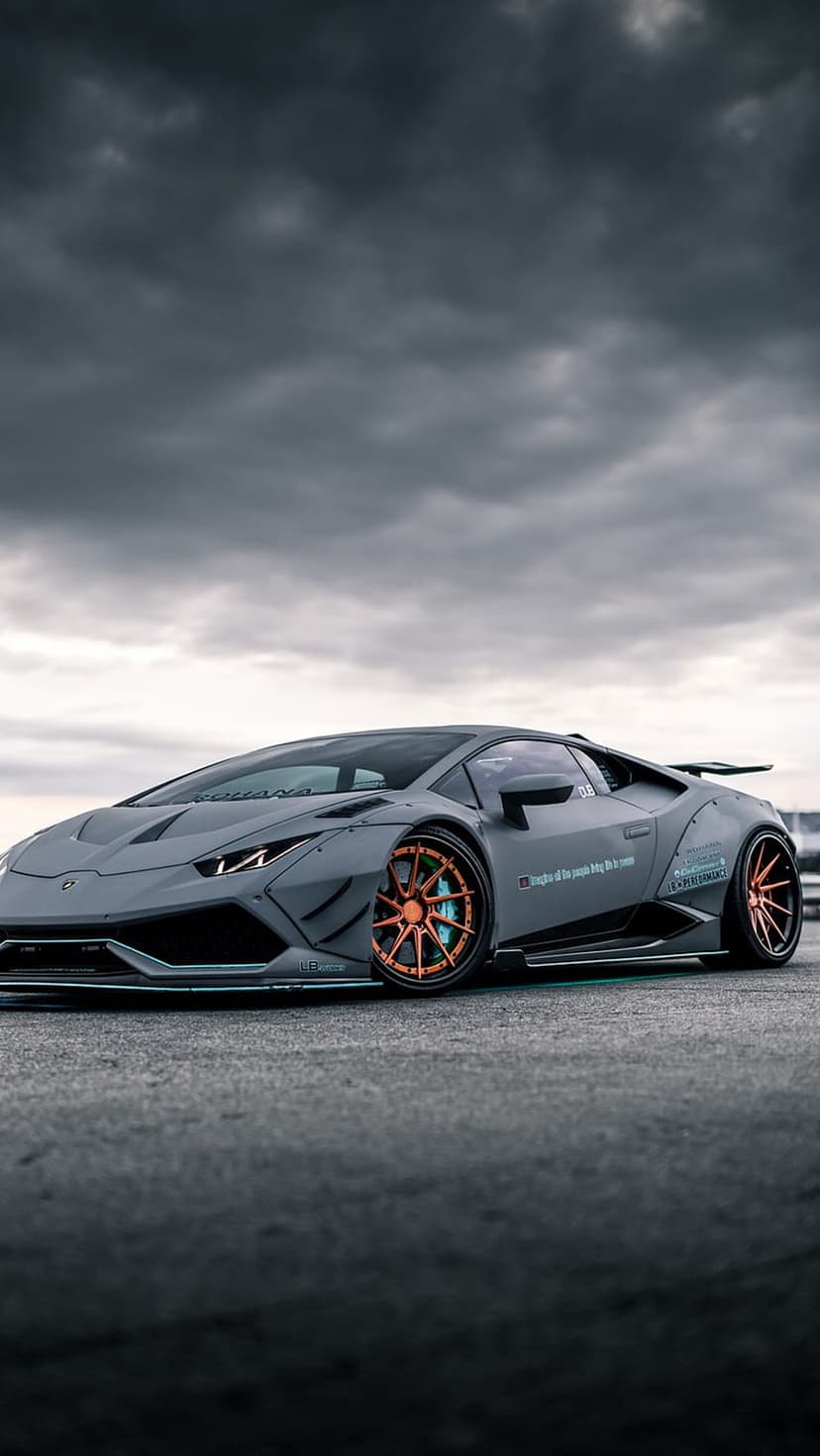 Grey Lamborghini Huracan with orange wheels and blue calipers beneath a moody sky for vertical mobile displays.