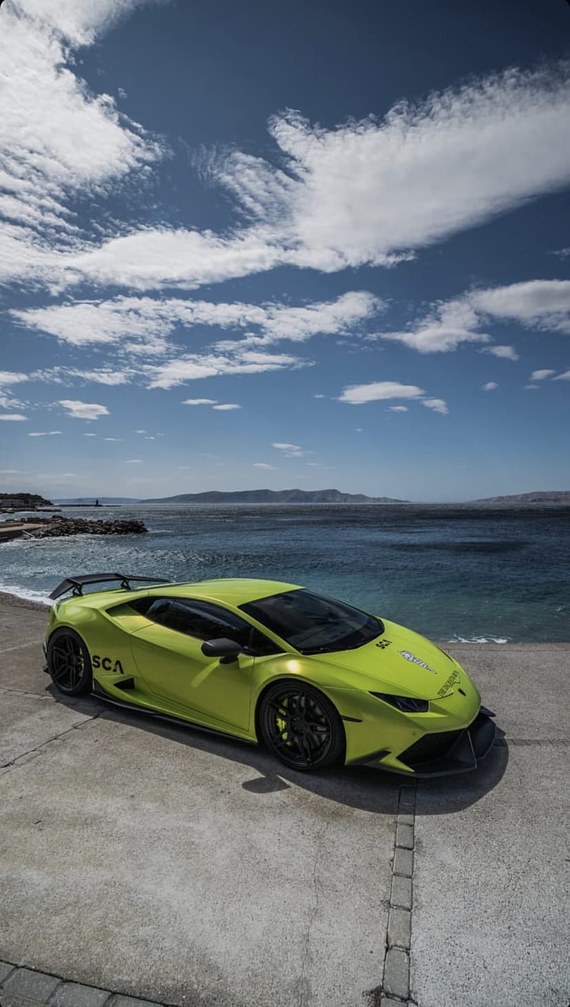 Lime green Lamborghini Huracan with black wheels parked on a concrete overlook against a blue ocean and sky.
