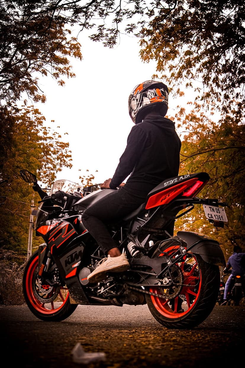 Biker on a KTM motorcycle viewed from behind against a backdrop of vibrant orange autumn forest trees.