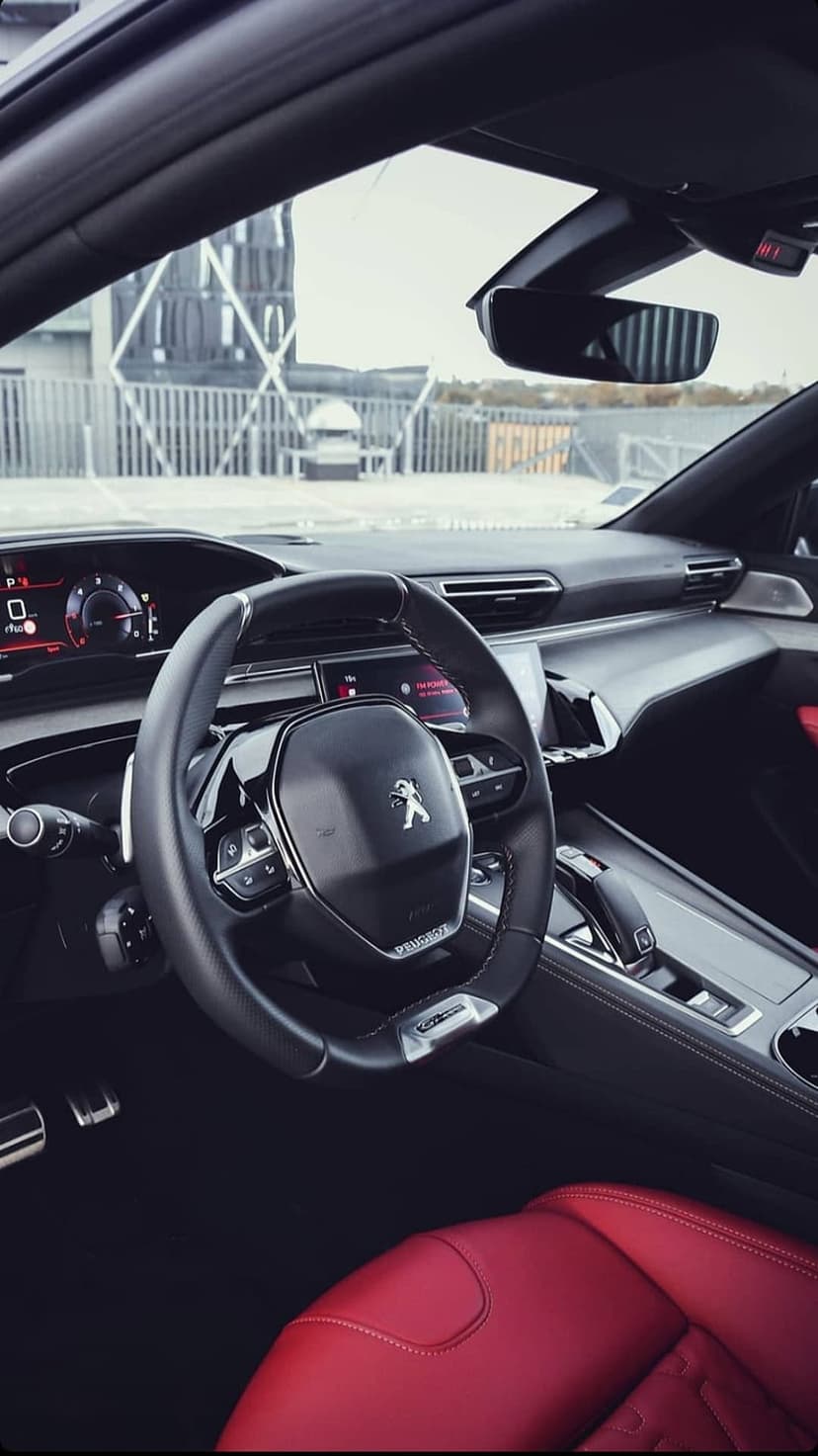 Red leather car seats and a digital dashboard inside a Peugeot 508 with a small steering wheel and tech display.
