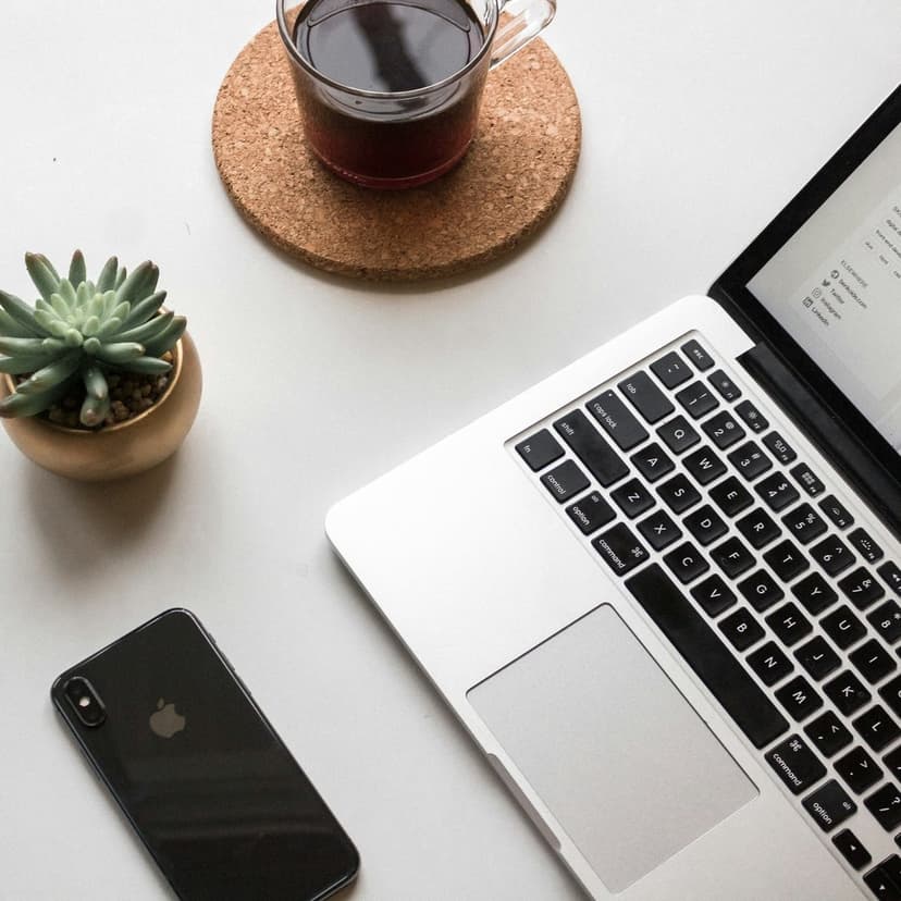 Laptop, glass coffee mug, and succulent plant on a white desk create a clean and productive workspace scene.
