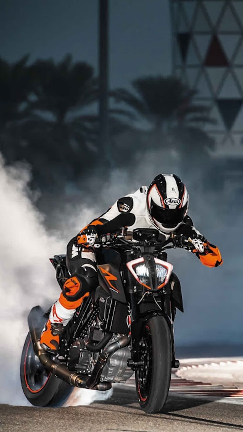 Motorcyclist in full gear performs a smoky tire burnout on a black and orange sportbike in a neon city setting.