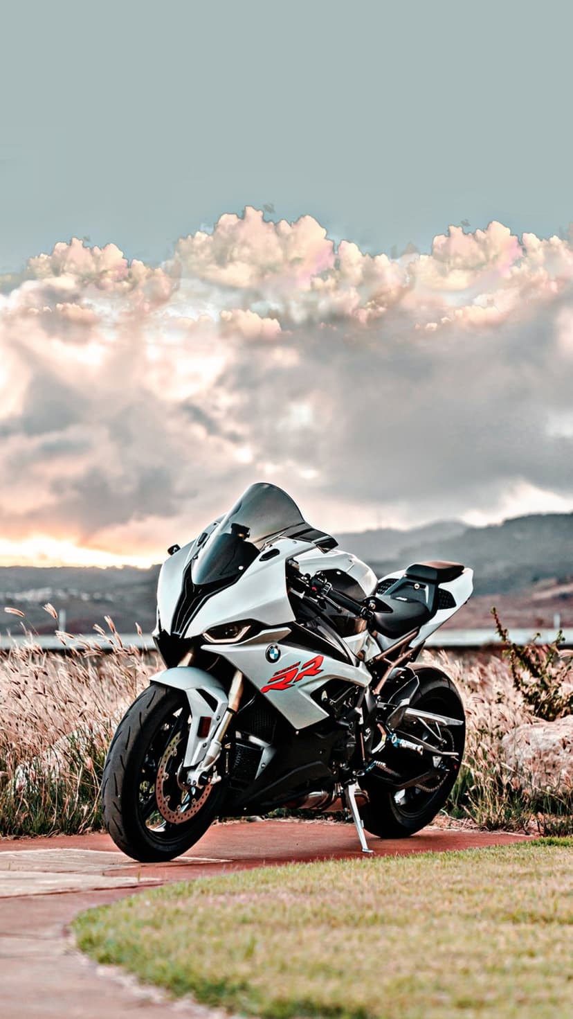 BMW S1000RR sportbike stands in dry grass before distant hills under a dramatic sky with soft clouds.