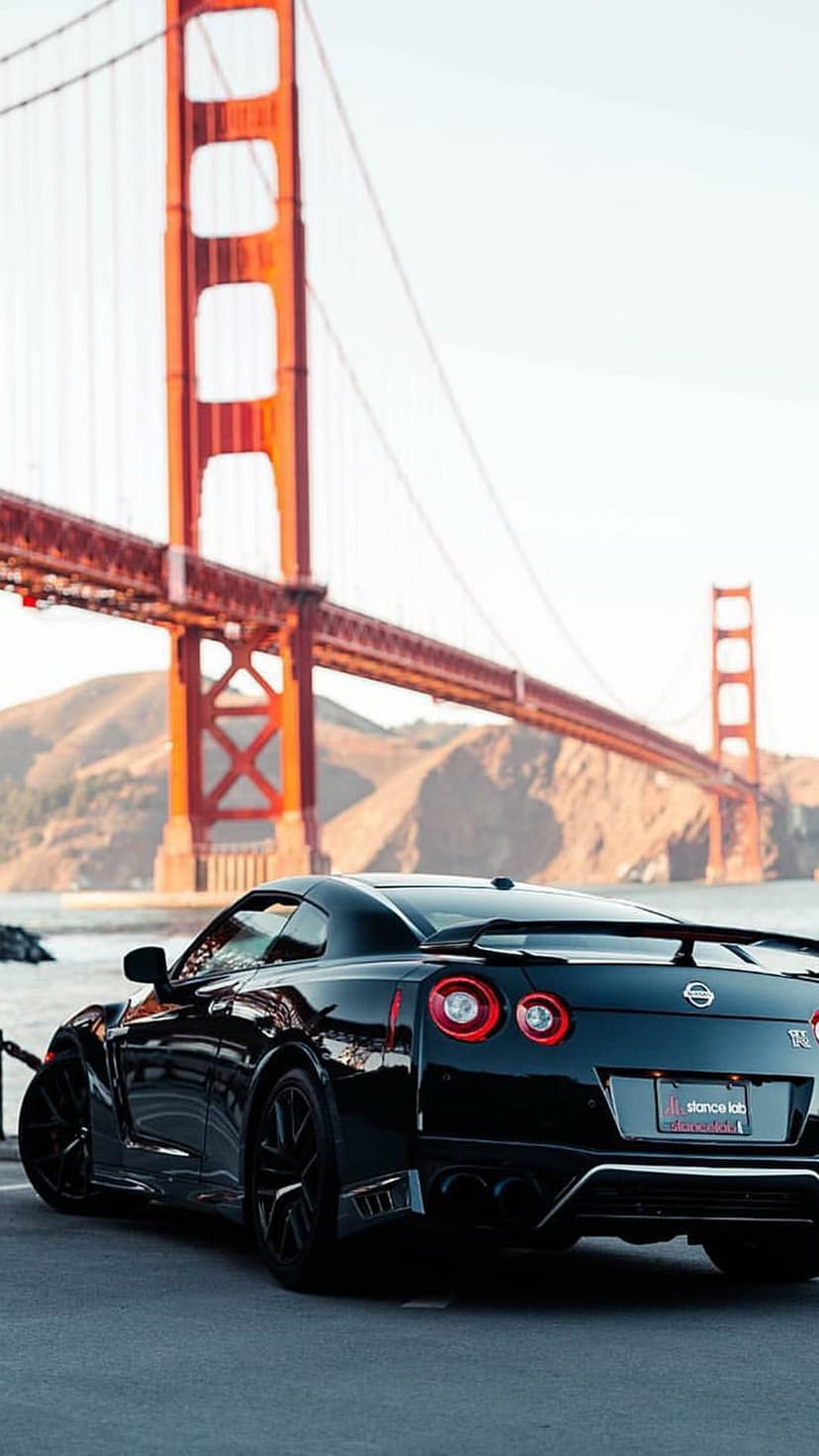 Black Nissan GT-R parked with the orange Golden Gate Bridge and blue sky visible in the background.