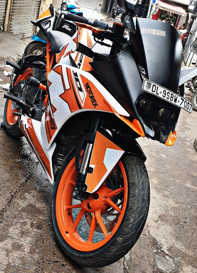 Orange KTM RC 390 motorcycle features a black windshield with bold white lettering and a custom license plate.