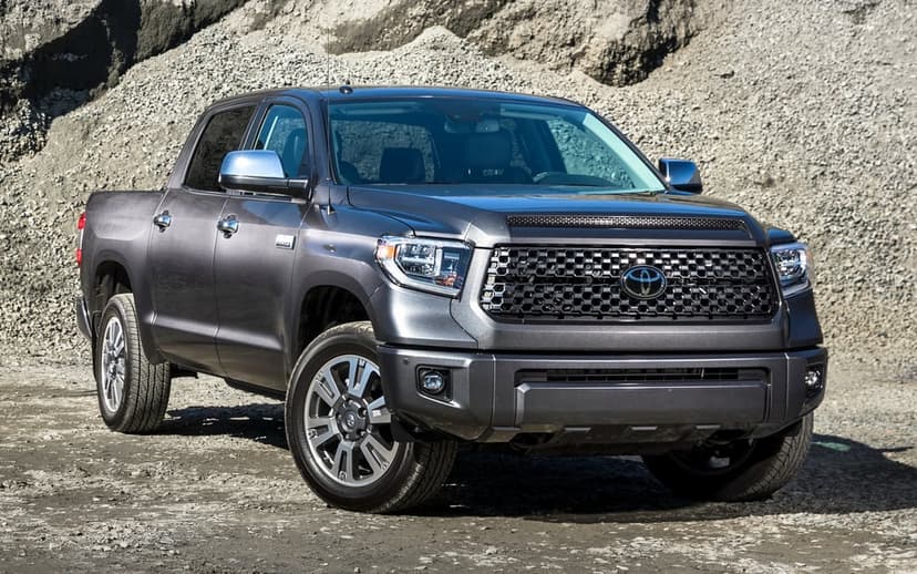 Dark grey Toyota Tundra pickup truck parked in a gravel quarry under bright natural daylight.