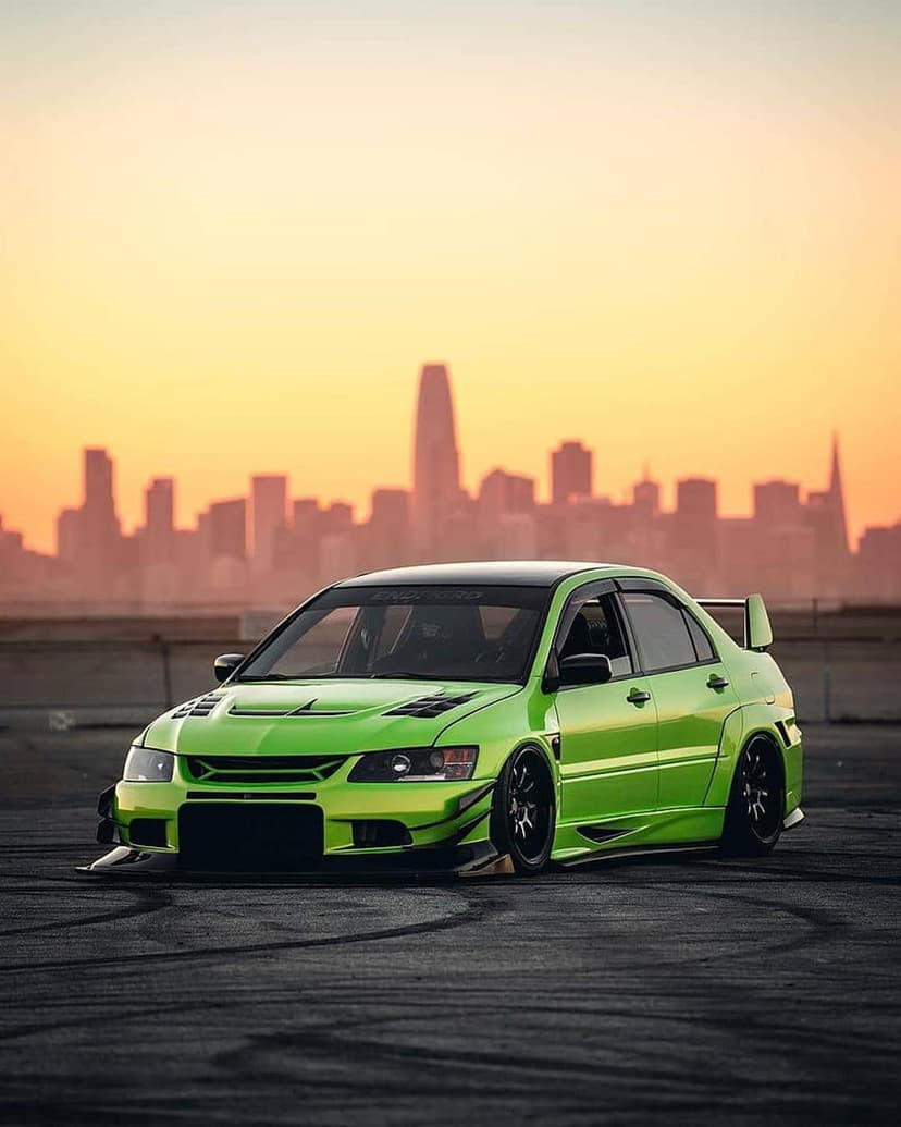 Neon green Mitsubishi Lancer Evolution X parked on asphalt with the San Francisco skyline under a sunset sky.