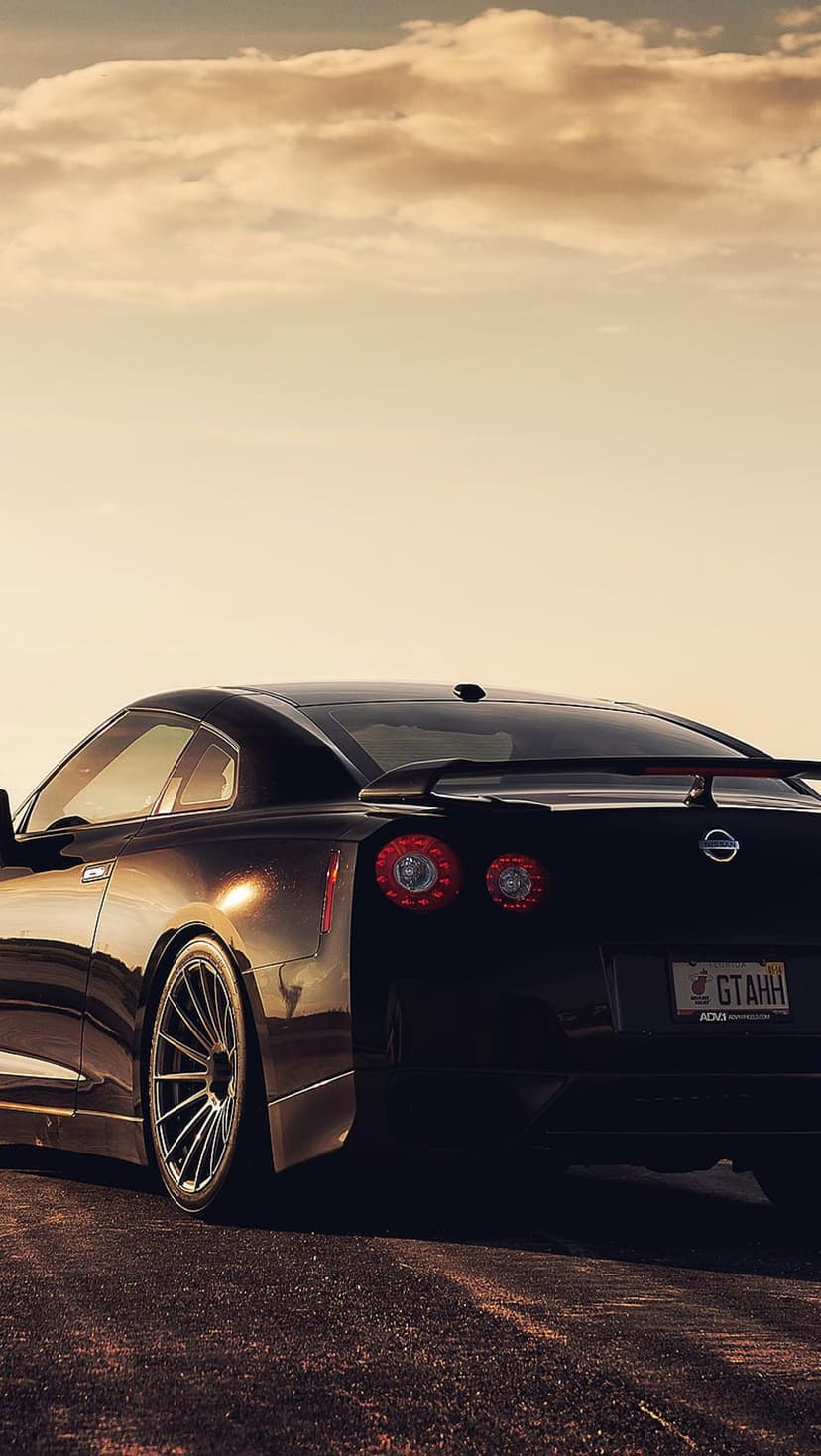 Black Nissan GT-R rear view with glowing red circular taillights under a dramatic orange and purple sunset sky.