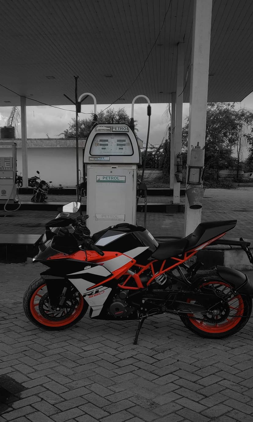 KTM RC sport motorcycle with orange accents parked beside a fuel pump under bright gas station lighting at night.