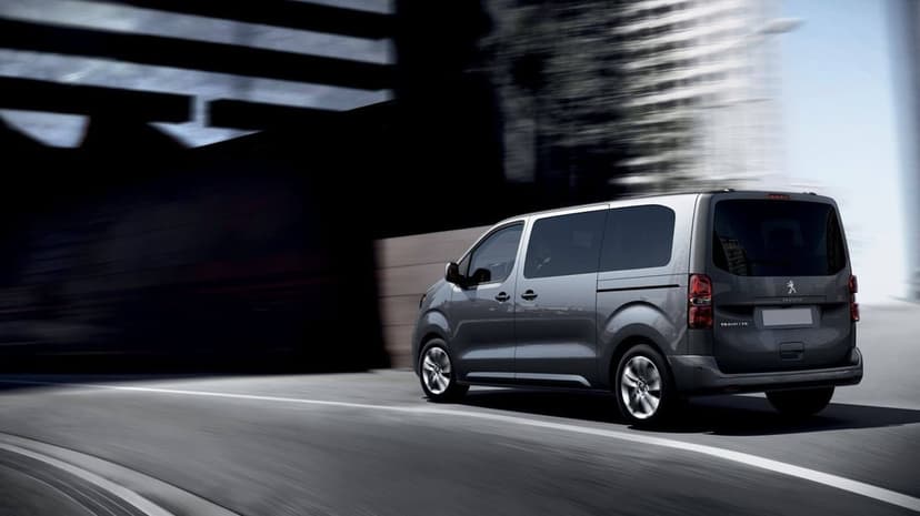 Grey Peugeot Traveller van driving on an urban road with motion blur and city buildings background.