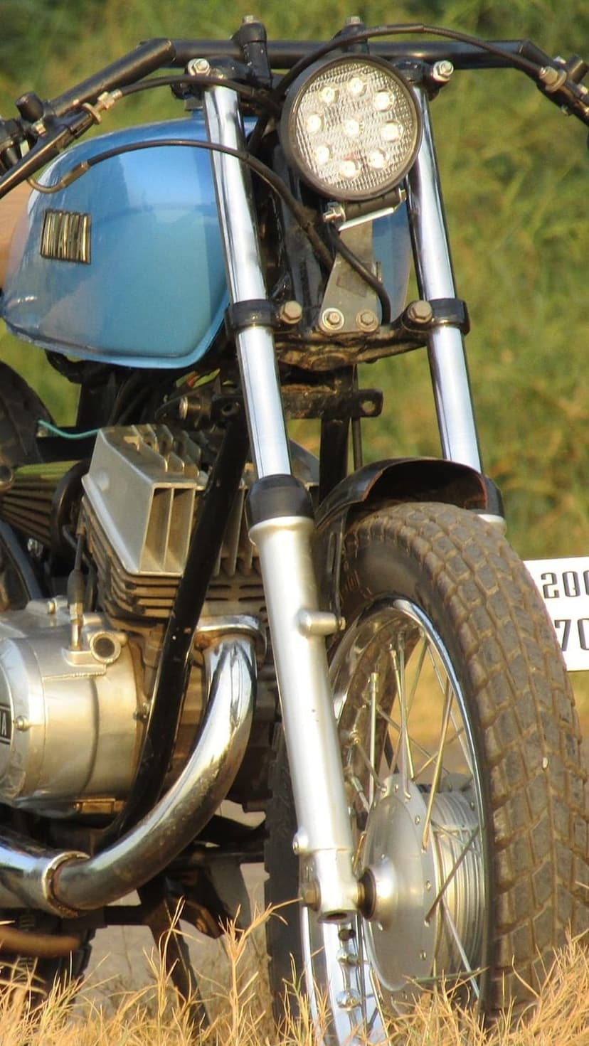 Blue Yamaha motorcycle fuel tank and LED headlight with chrome exhaust pipes and knobby tires in a close-up shot.