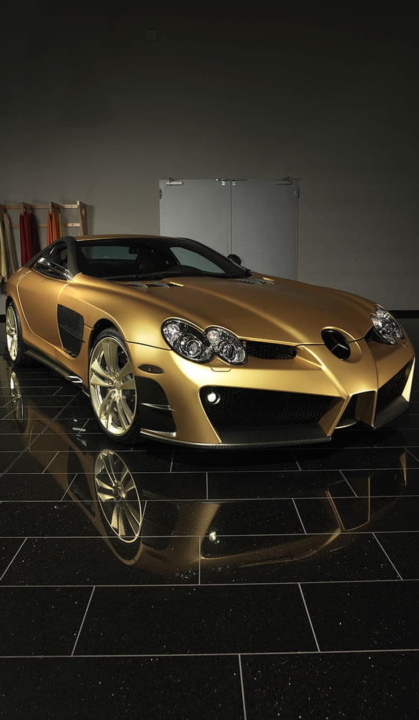 Golden Mercedes-Benz SLR McLaren supercar reflecting on a glossy black studio floor with sharp headlights visible.