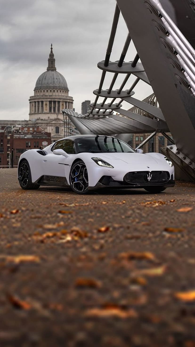 White Maserati MC20 on Millennium Bridge with autumn leaves and St. Paul's Cathedral dome in the background.