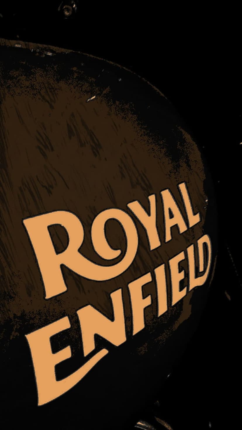 Royal Enfield logo in light orange text on a dark, textured motorcycle fuel tank with a vintage aesthetic.