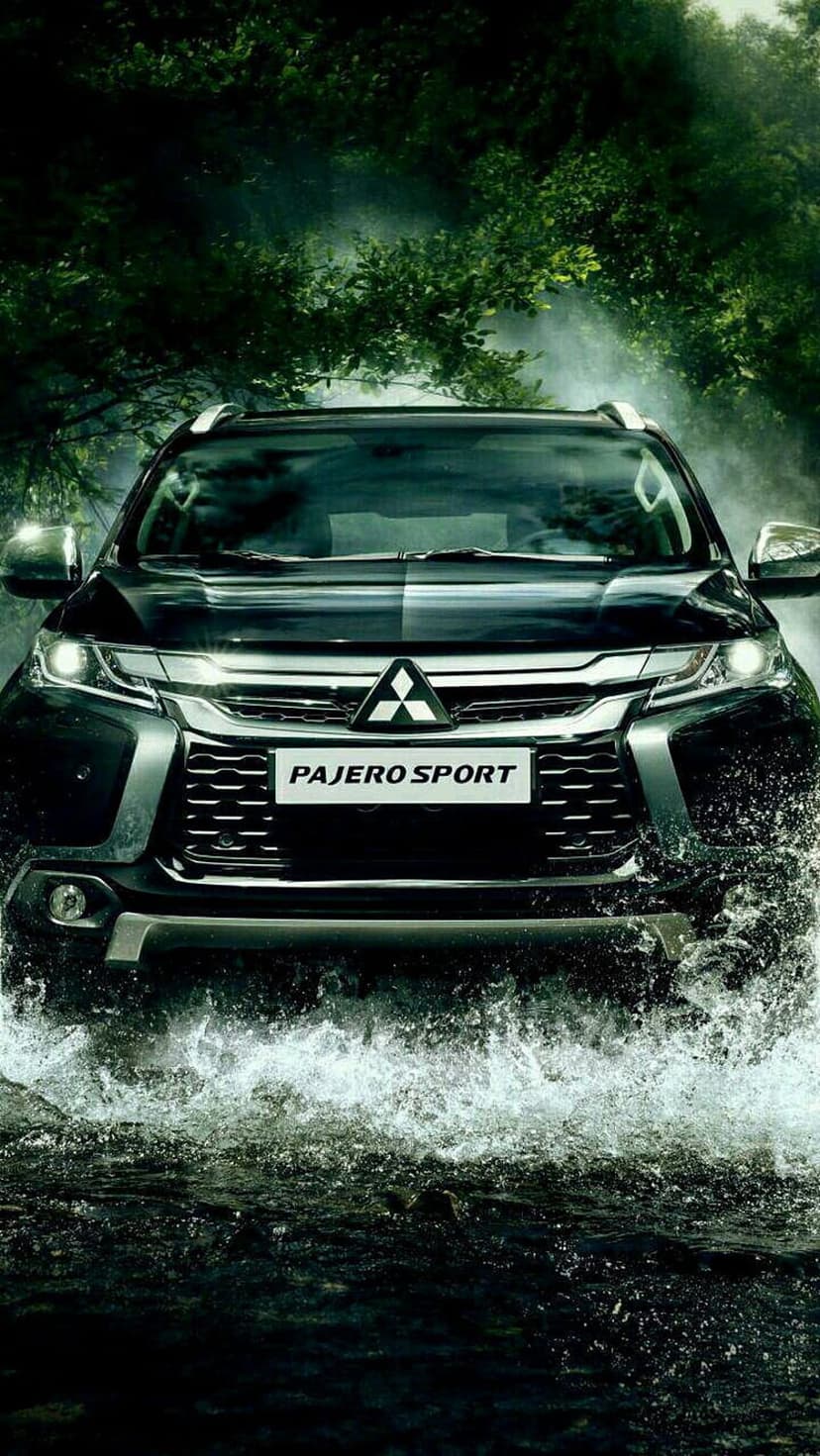 Mitsubishi Pajero Sport SUV driving through a forest stream with water splashing around the tires and green trees.