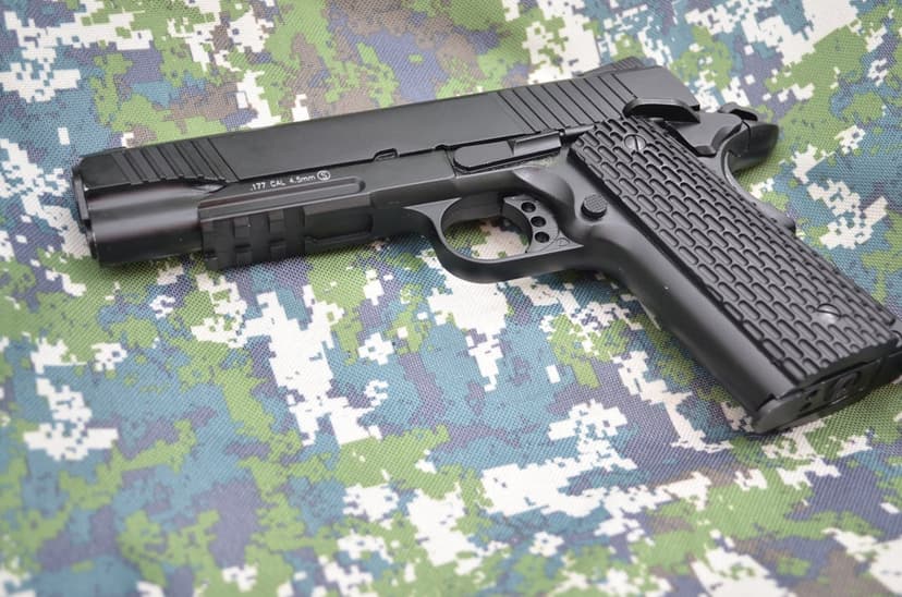 Black semi-automatic handgun with a textured grip rests on green and brown digital camouflage tactical fabric.