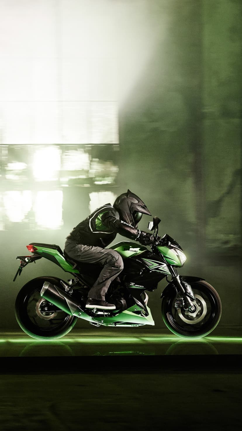 Kawasaki motorcyclist in black gear leans into a turn with glowing green light streaks on a dark road.