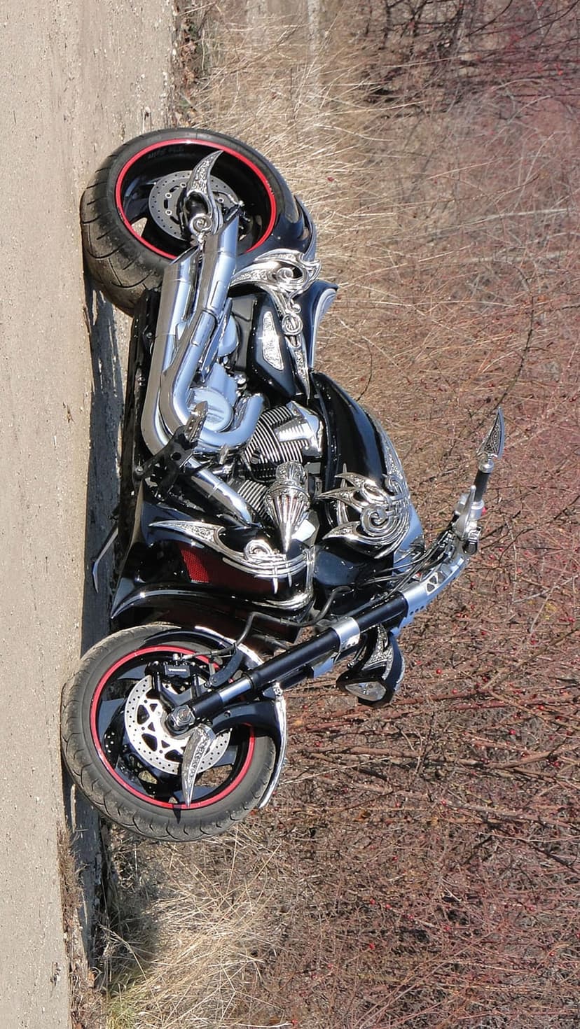 Black chopper motorcycle featuring red rim accents and chrome engine components on a rustic dirt path backdrop.
