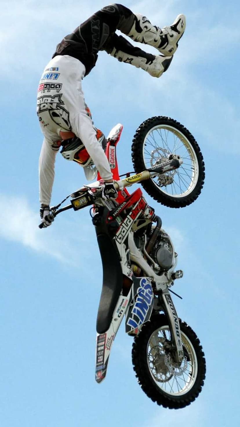 Motocross rider executes a vertical backflip on a dirt bike against a clear blue sky during an aerial stunt.