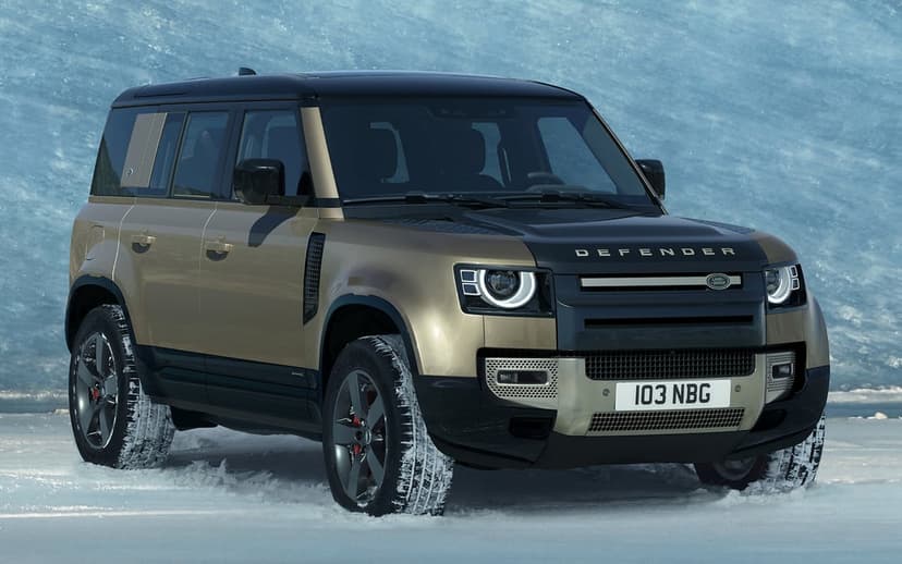 Land Rover Defender in gold and black parked on snow with an icy blue background and glowing headlights.