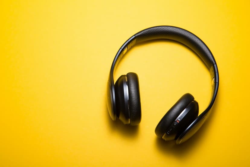 Black wireless headphones rest on a solid bright yellow surface in a clean, minimalist overhead composition.