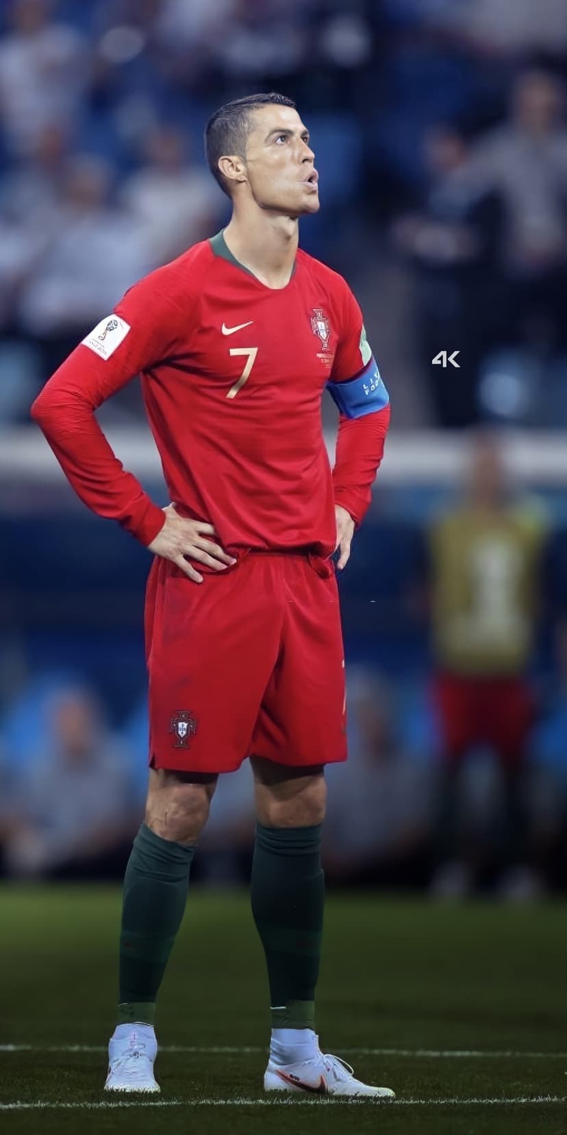 Cristiano Ronaldo stands on a soccer pitch wearing a red Portugal jersey and shorts while looking up at the sky.