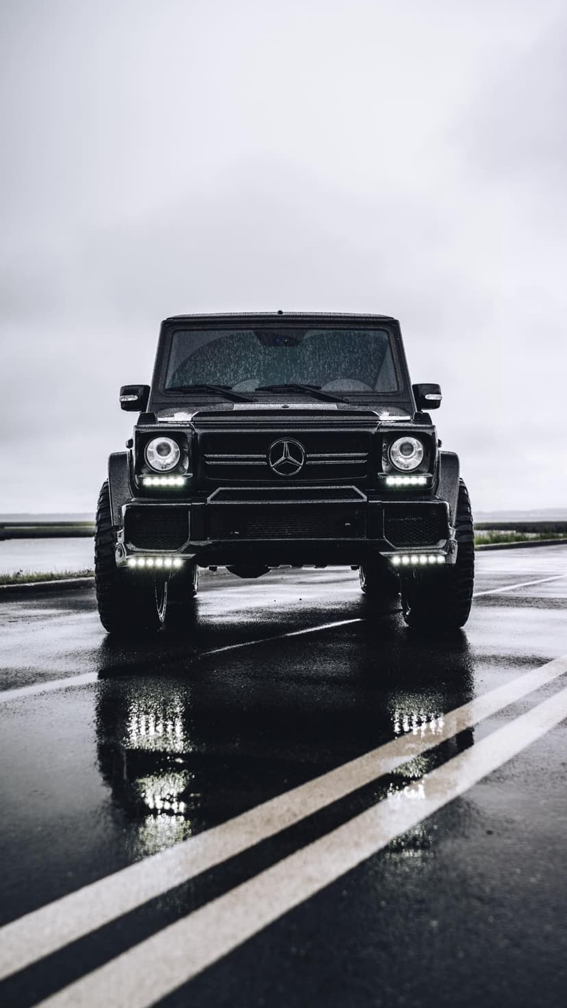 Front view of a black Mercedes-Benz G-Class with glowing LED lights reflecting on a glistening wet rainy road.