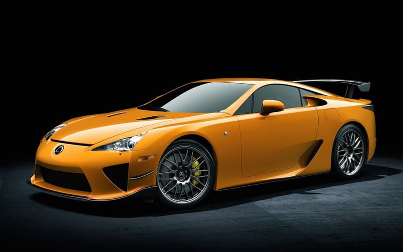 Orange Lexus LFA Nurburgring Edition supercar with a large rear wing on a dark studio floor and background.