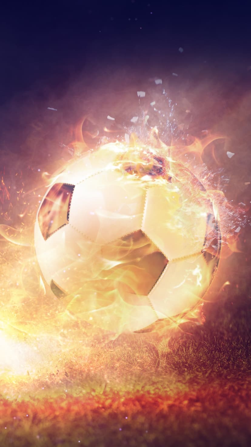 Soccer ball engulfed in orange flames and flying sparks over a dark grass field with high contrast lighting.