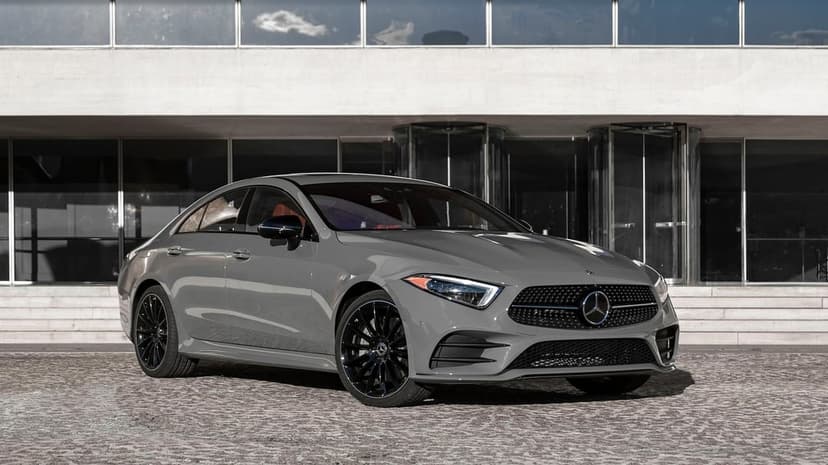 Grey Mercedes-Benz CLS with black wheels parked on cobblestone in front of a glass and concrete building.