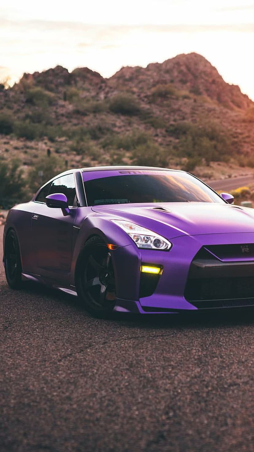 Nissan GT-R with a matte purple finish parked on a desert highway under a glowing orange sunset sky.