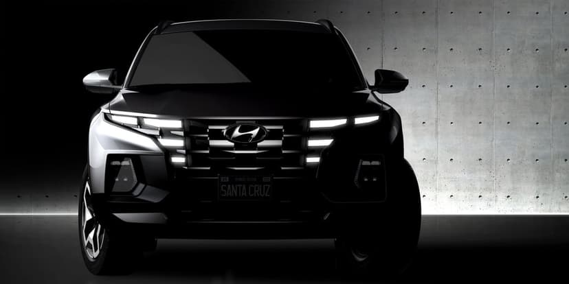 Front view of a black Hyundai Santa Cruz with glowing LED headlights against a gray concrete wall background.