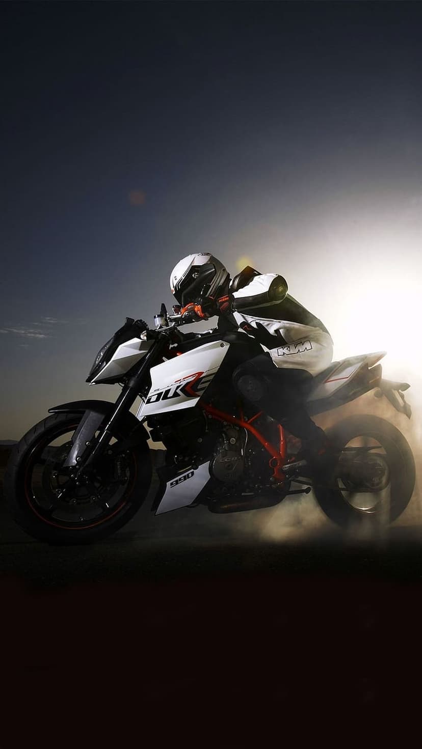 Motorcycle rider on a KTM Duke leans into a sharp turn as dust and smoke billow under a bright sunlit sky.