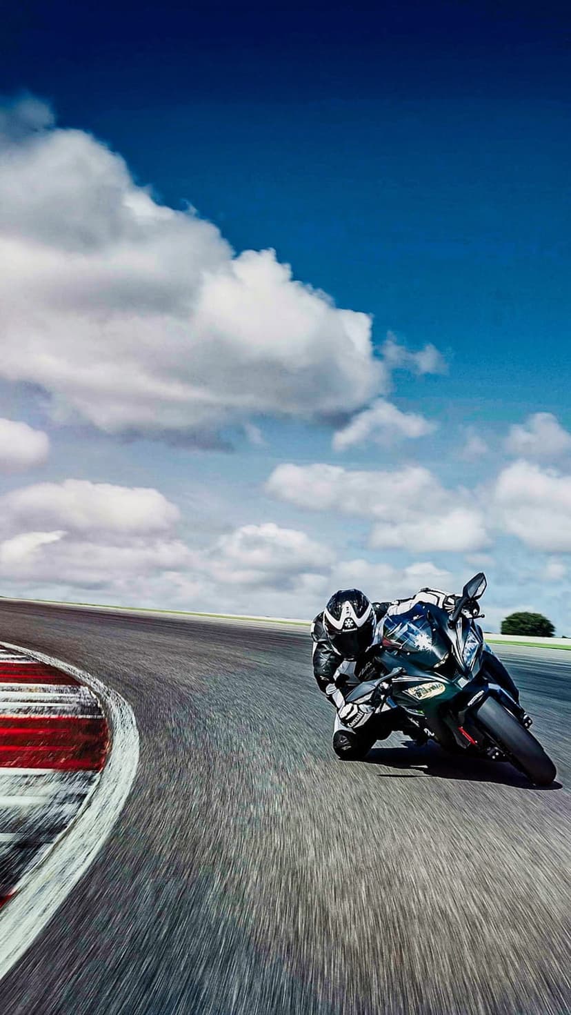 Motorcyclist wearing racing leathers leans deep into a turn on a sunlit track with blurred asphalt background.