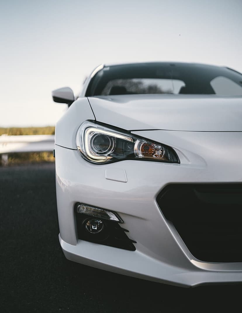 White sports car headlight and front grille featuring sharp lines and a dark asphalt ground contrast.