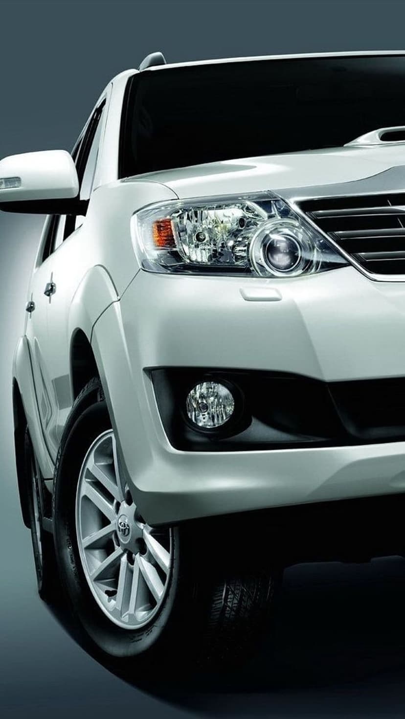 White Toyota Fortuner SUV displays sleek LED headlights and a bold front grille in a vertical close-up angle.