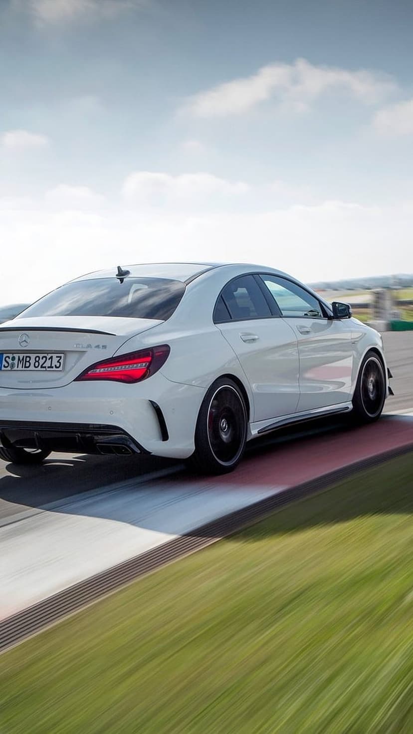 White Mercedes CLA 45 AMG rear view showing spoiler and taillights on a blurred racetrack circuit.