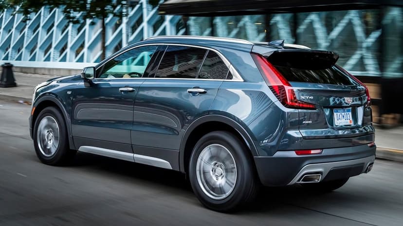 Rear profile of a dark blue Cadillac XT4 SUV driving on a city street with motion blurred background and wheels.