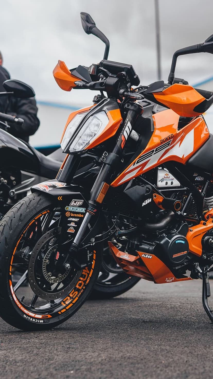 KTM 125 Duke front fender and wheel rim with orange accents and racing stickers on dark outdoor asphalt.