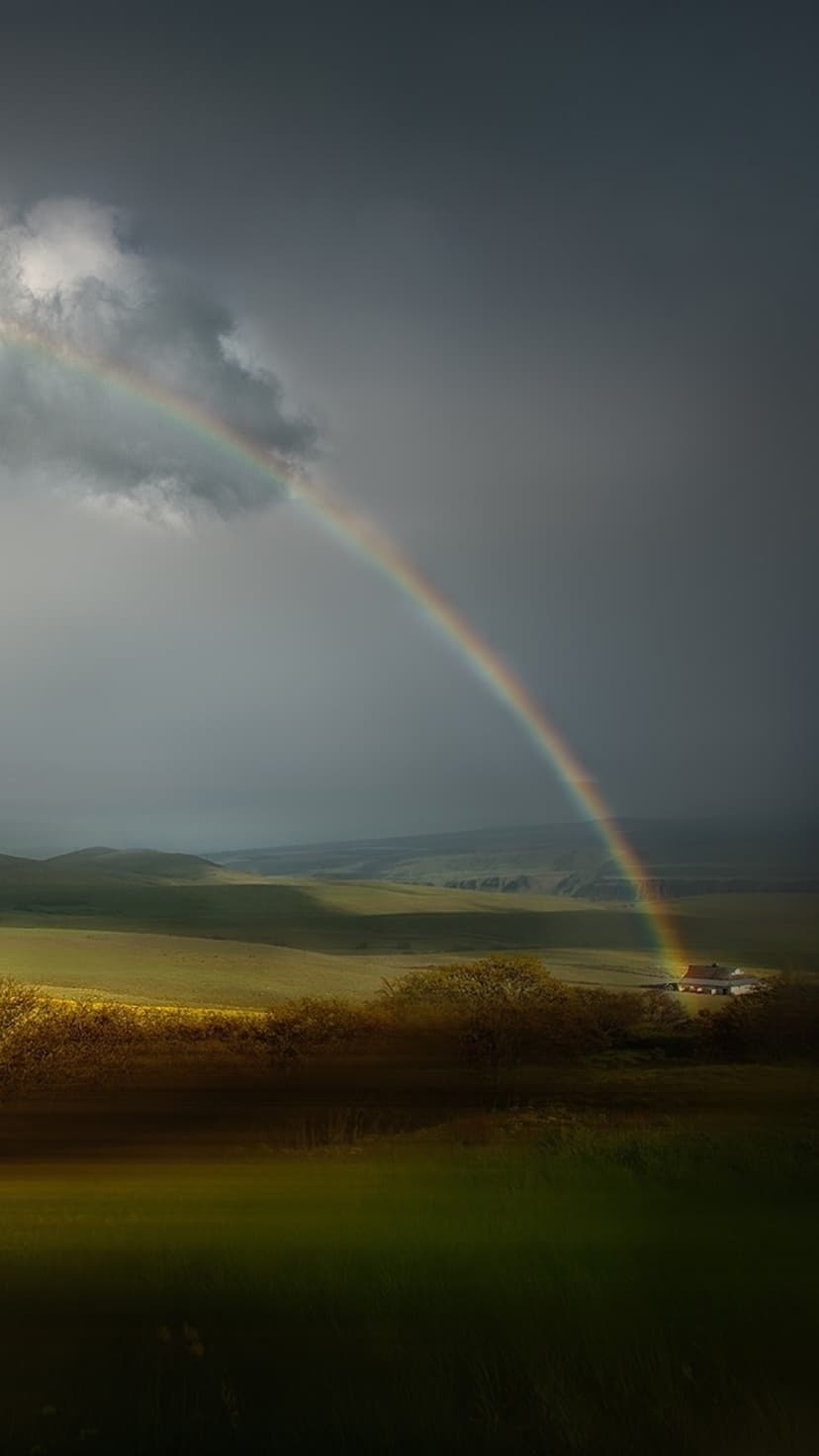 Colorful rainbow arches over a stormy sky and green rolling hills with a small white farmhouse in the distance.