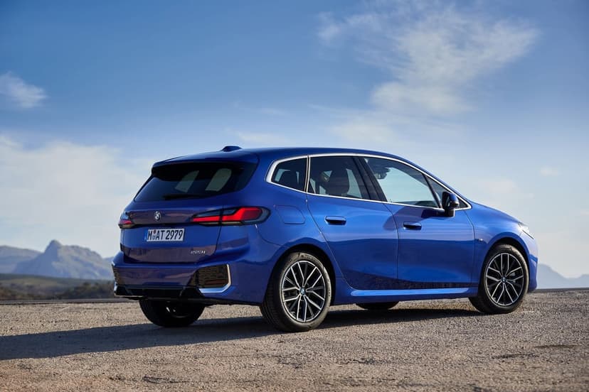 Blue BMW 223i Active Tourer parked on a gravel road with mountains and a clear blue sky in the distance.
