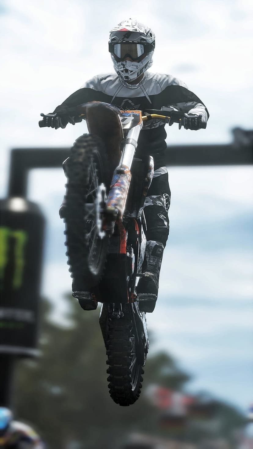 Motocross rider in full protective gear performs a high-altitude jump on a dirt bike over an outdoor race track.