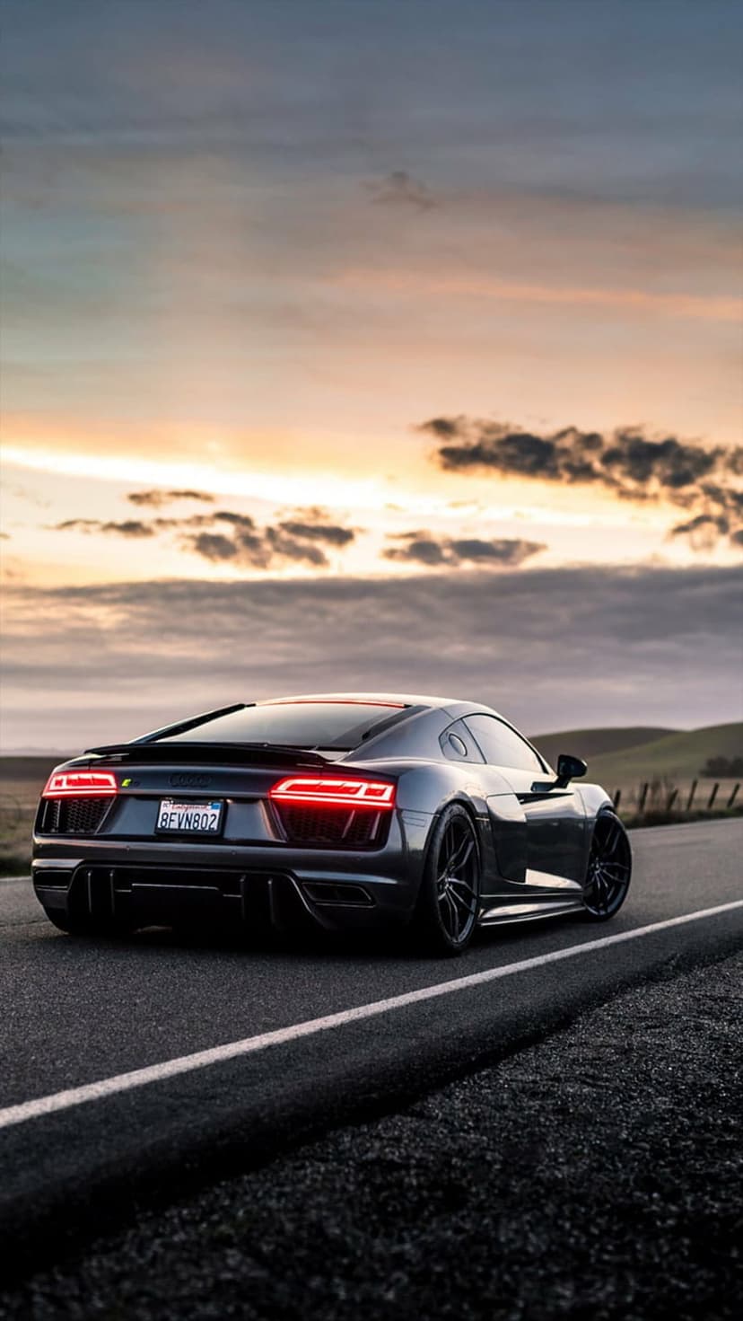 Audi R8 rear view on a highway under a fiery orange sunset with glowing LED taillights and rolling hills.