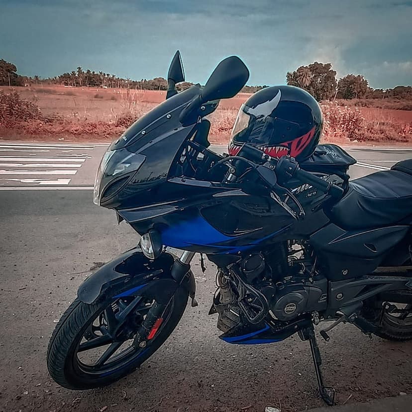 Venom-themed helmet on a blue sport motorcycle parked by a pedestrian crossing under a cloudy rural sky.